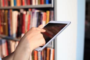osoba trzymająca tablet na tle półki z książkami