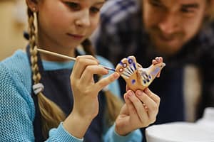 Warsztaty - dziewczynka maluje glinianego ptaka.