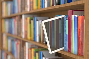Czytnik ebooków wsunięty pomiędzy książki na bibliotecznym regale.